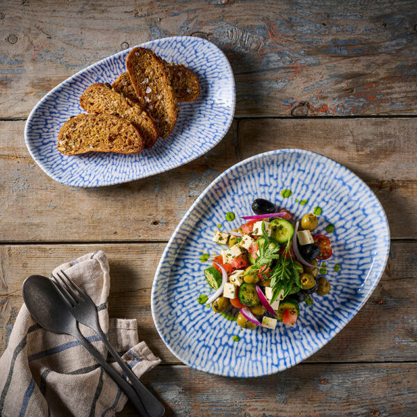 Churchill Inked Cascade Indigo Opal Platter und Natural Platter mit einem mediterranen Salat, präsentiert auf einem braunen Tisch.