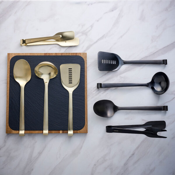 Black and Gold Comas Utensils arranged on a Comas Slate Board, placed on a marble tabletop